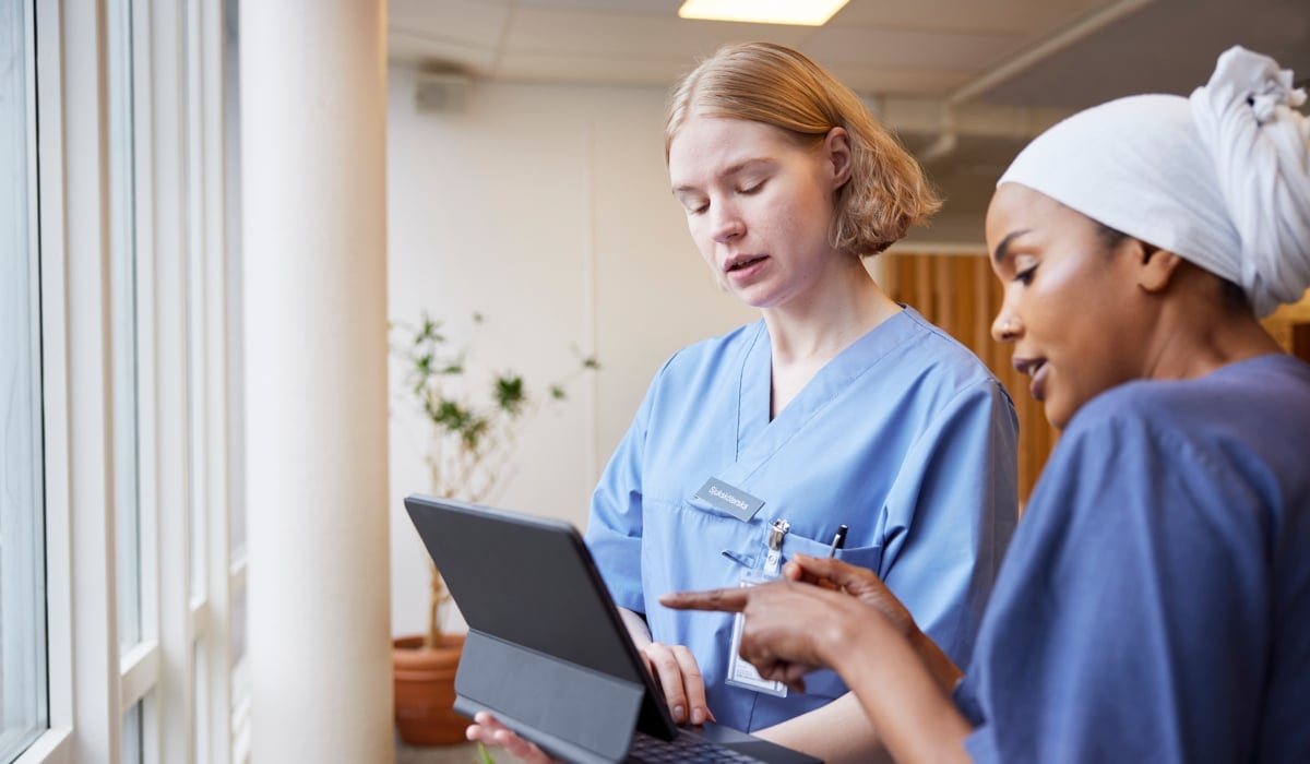 Två kvinnor i vårdkläder tittar på en bärbar dator.