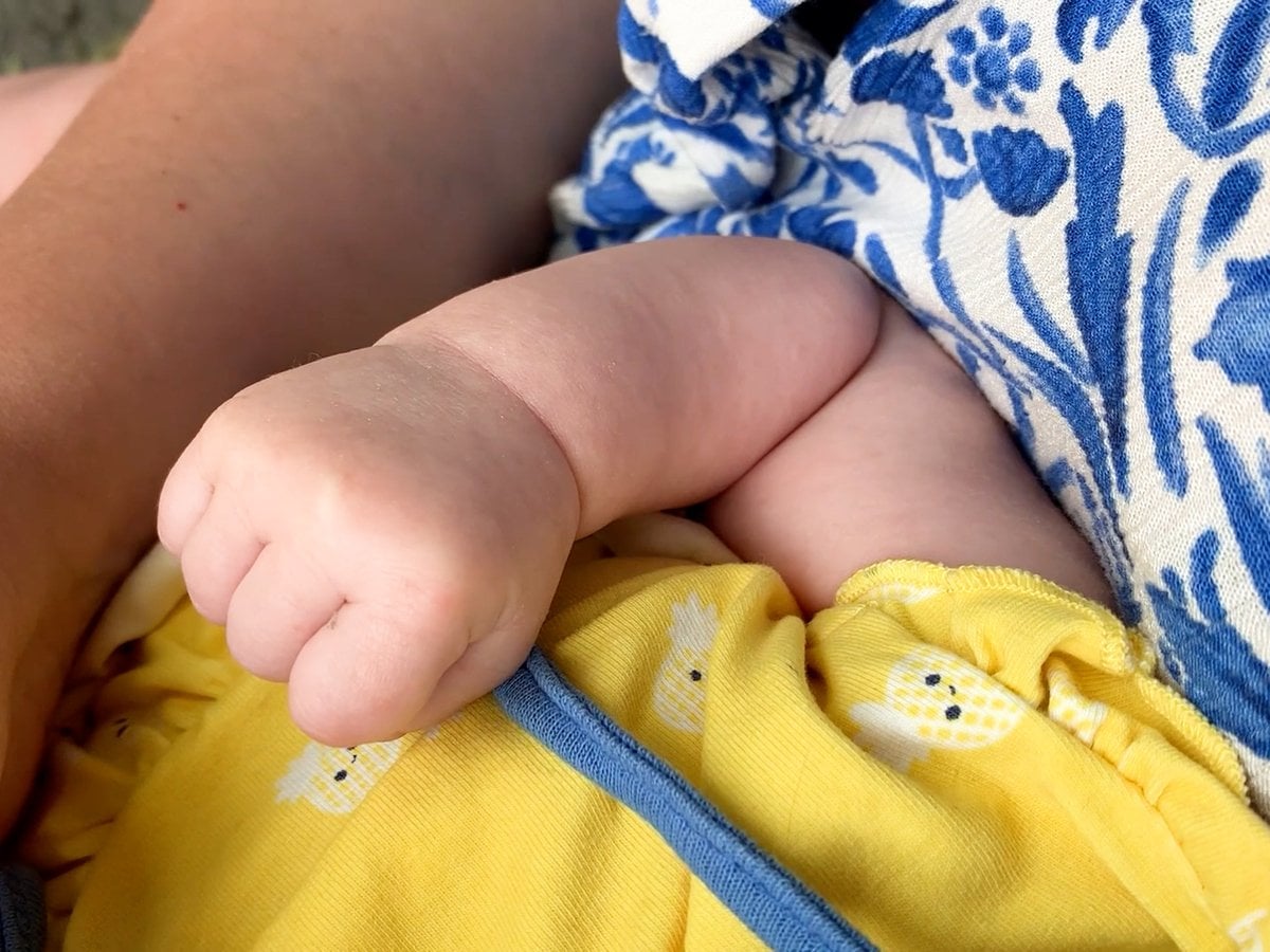 En person håller en bebis i famnen. Bilden fokuserar på bebisens arm och hand.