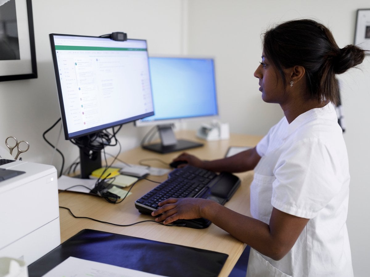 Sjukvårdspersonal som står vid ett skrivbord och tittar på en datorskärm.